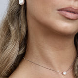 Close-up of a woman wearing pearl earrings and a necklace with a plain background